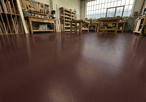 Lśniąca podłoga w kolorze RAL 8017, o gładkiej powierzchni, odbija światło i zarysy wyposażenia.