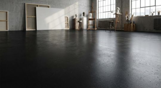 Przestronne, nowoczesne studio artystyczne z surowymi betonowymi ścianami i lśniącą, ciemną podłogą w kolorze RAL 9005.